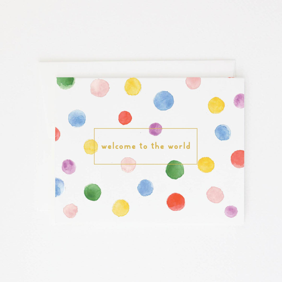 Greeting card with colorful polka dots and 'welcome to the world' text in gold foil on a white background