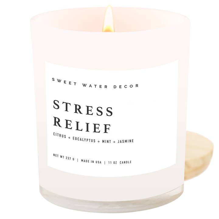 Lit candle in opaque container with white label next to wooded lid.