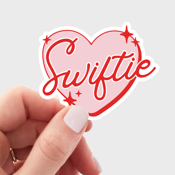 Pink heart-shaped sticker with 'Swiftie' text in red.