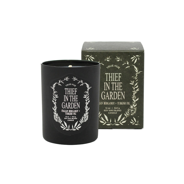True Hue Thief in the Garden candle in black container with decorative label next to a matching box.