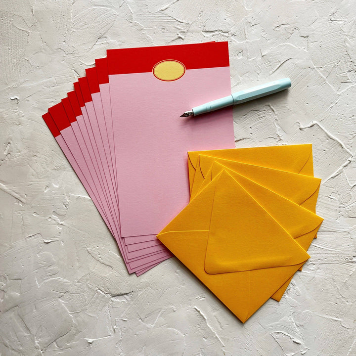 Eight sheets of pink paper fanned on top of yellow envelopes. Each sheet has a red band at the top and the drawing of an oval label. 