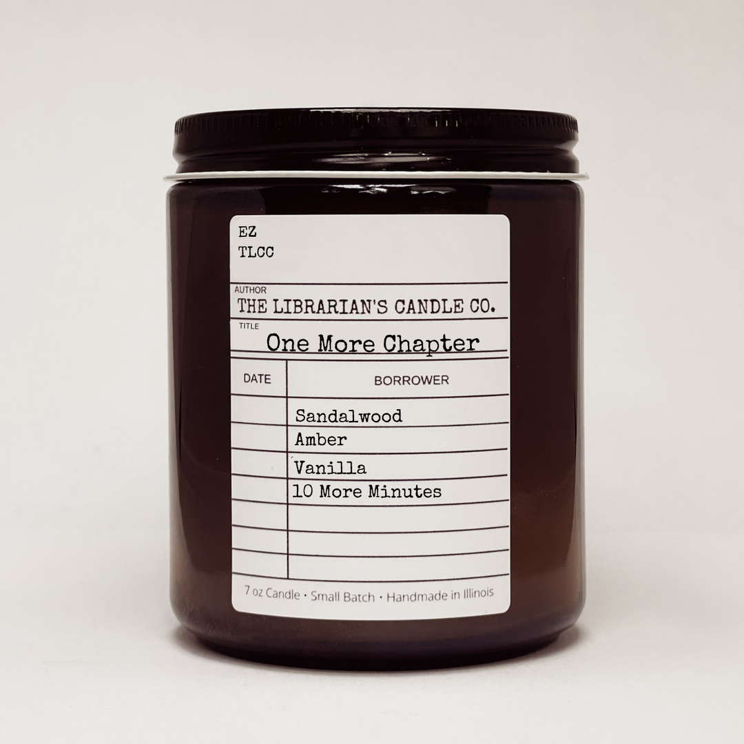 Candle jar with a label in the design of a library due date slip for the book 'One More Chapter' detailing scent notes: sandalwood, amber, vanilla. 