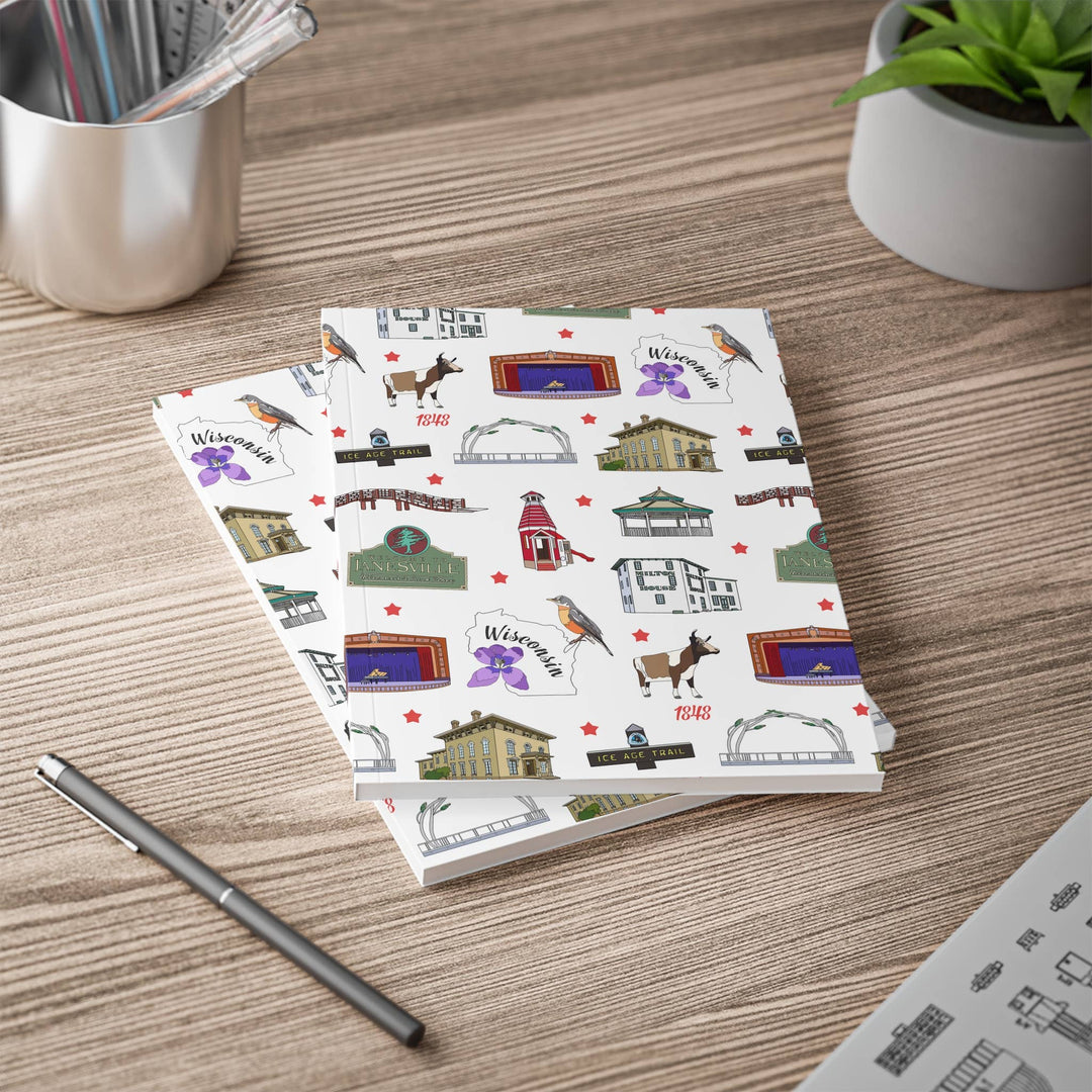 Two notebooks on a desk with plant and pencil. The notebook covers are filled with Janesville landmarks.