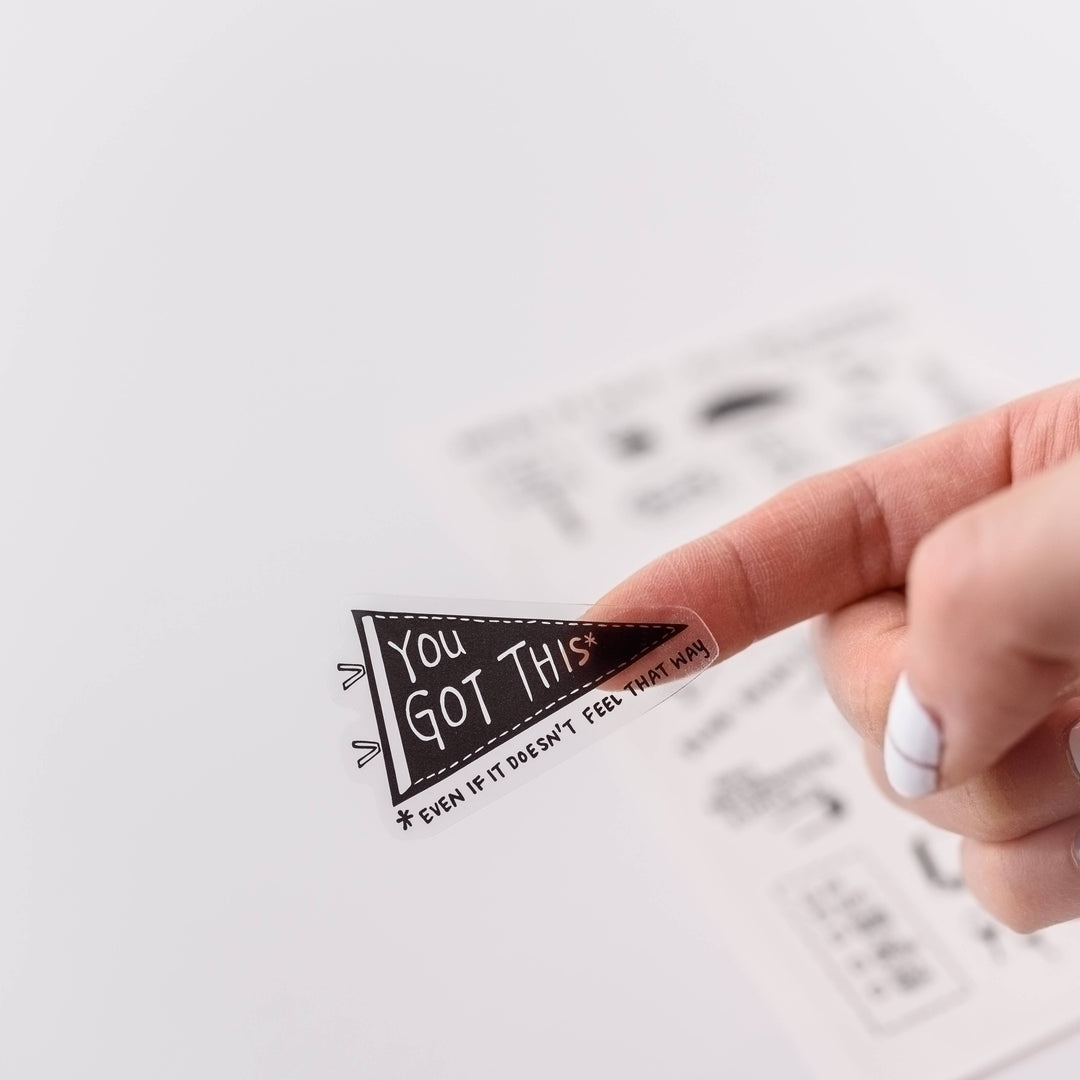 A finger holding a sticker in the shape of a pennant with the text "You Got This* *even if it doesn't feel that way."