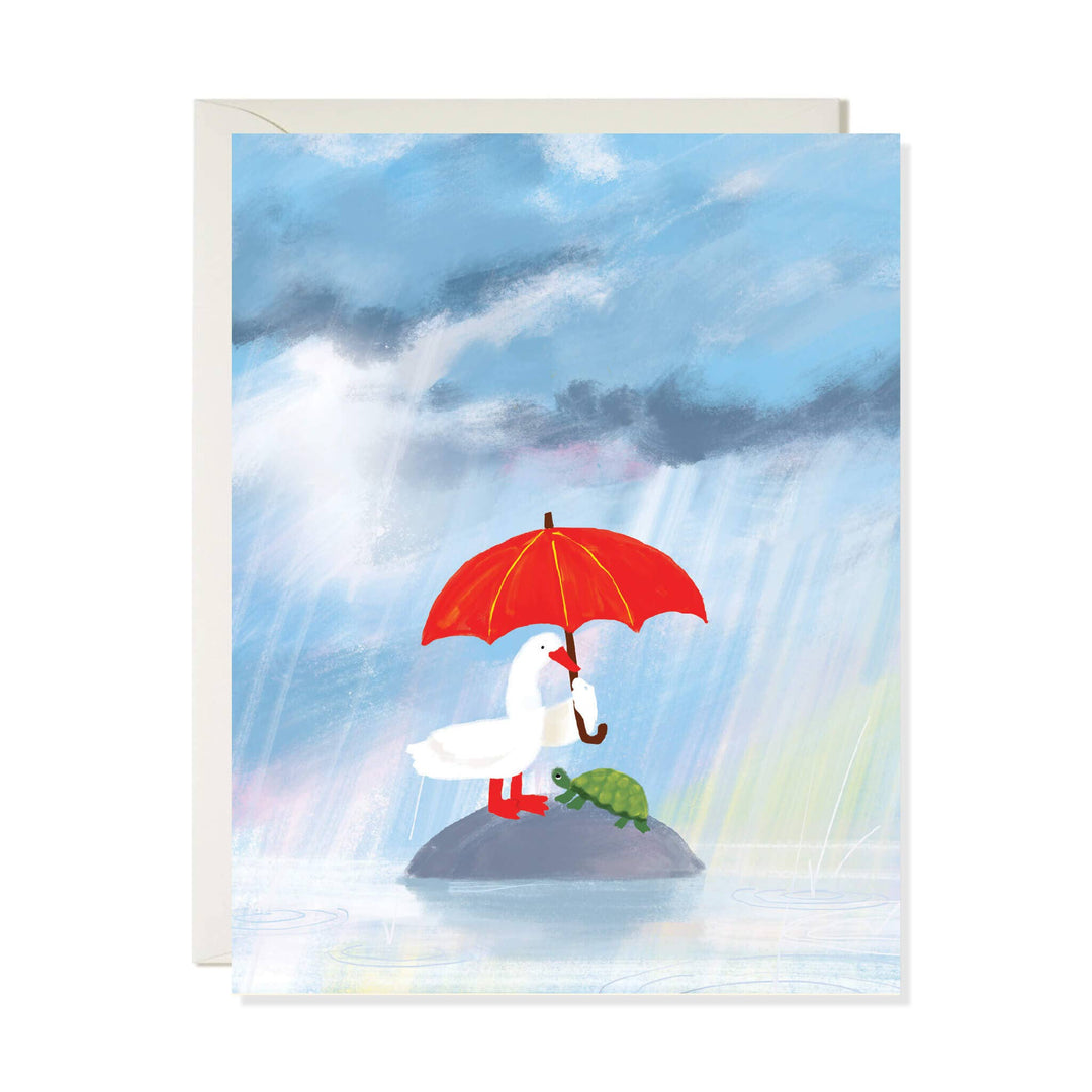 A greeting card with a white envelope, featuring an illustration of a white goose holding a red umbrella on a rock in the rain, with a small green turtle beside it.