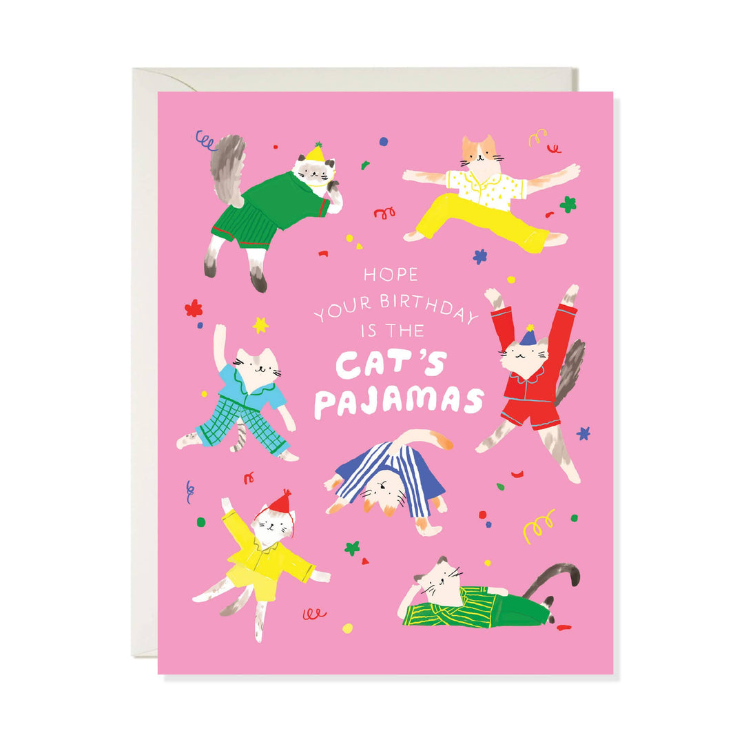 A pink greeting card with illustrated cats in colorful pajamas and the text 'HOPE YOUR BIRTHDAY IS THE CAT'S PAJAMAS', shown with a white envelope behind it.