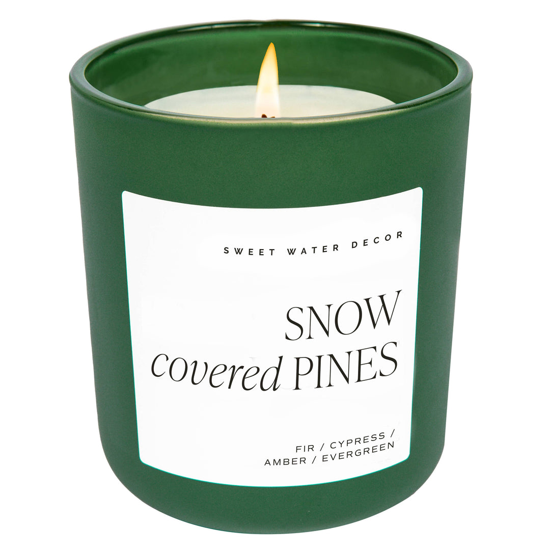 Scented soy candle in green matte glass container. Label is Snow Covered Pines  Fir / Cypress / Amber / Evergreen