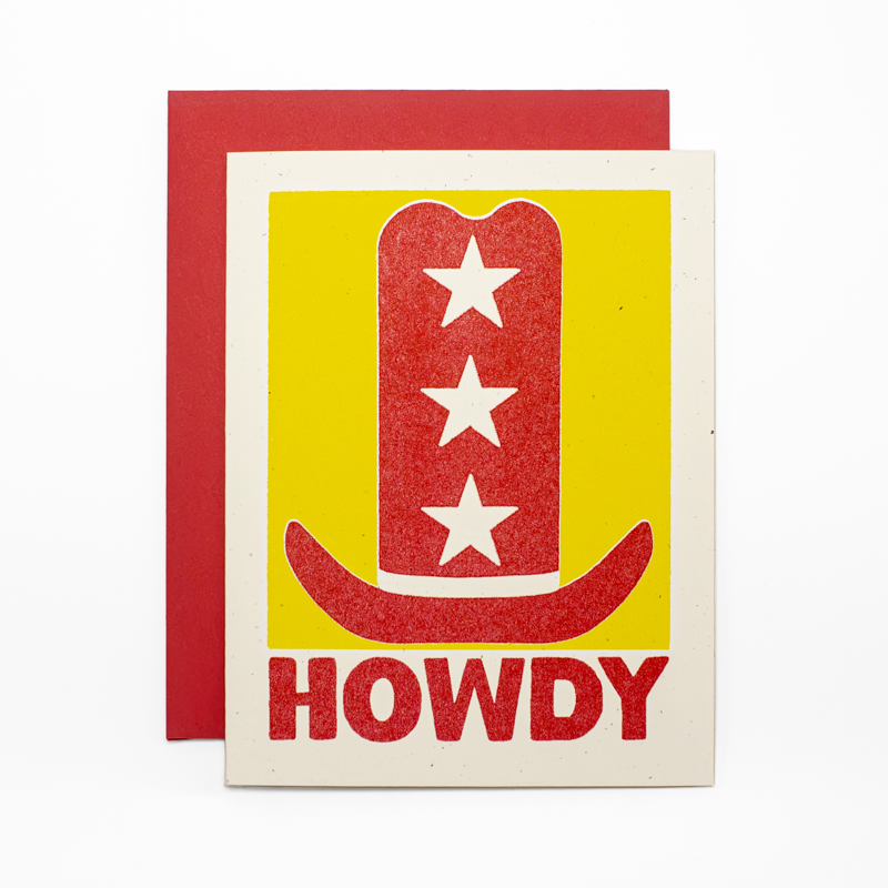 A greeting card with a red glitter cowboy hat graphic on a yellow background, with the word 'HOWDY' in red at the bottom, shown with a red envelope behind it.