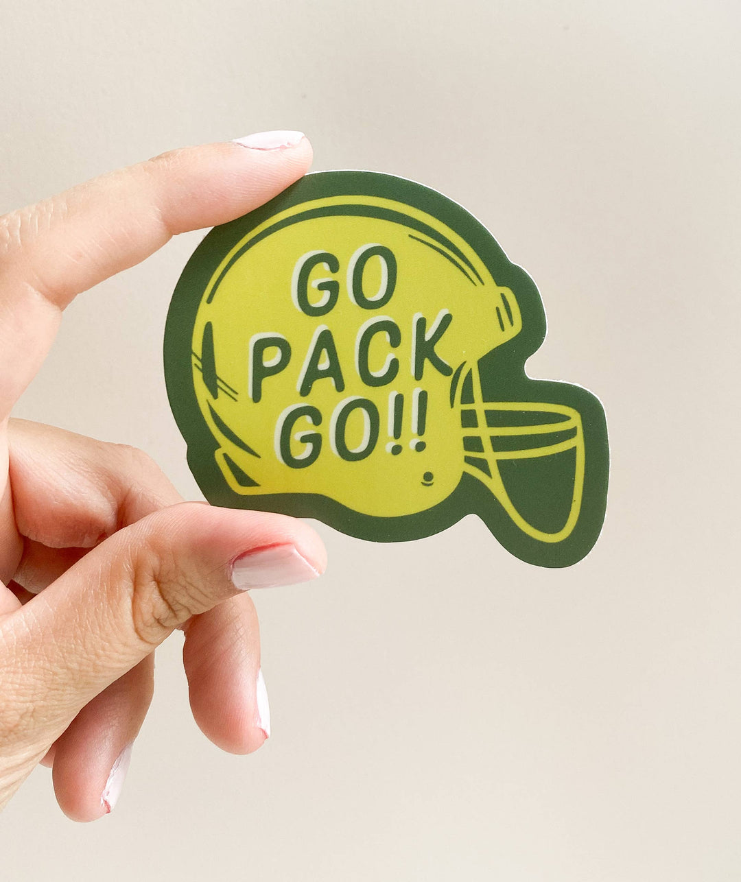 Hand holding a sticker in shape of football helmet in Green Bay Packers colors with the text "Go Pack Go".