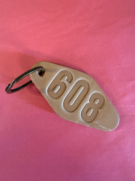 Brown leather keychain in a classic hotel keyring shape with "608" stamped in large letters.