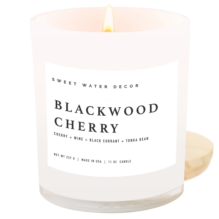 Lit candle in opaque container with white label next to its wooden lid.