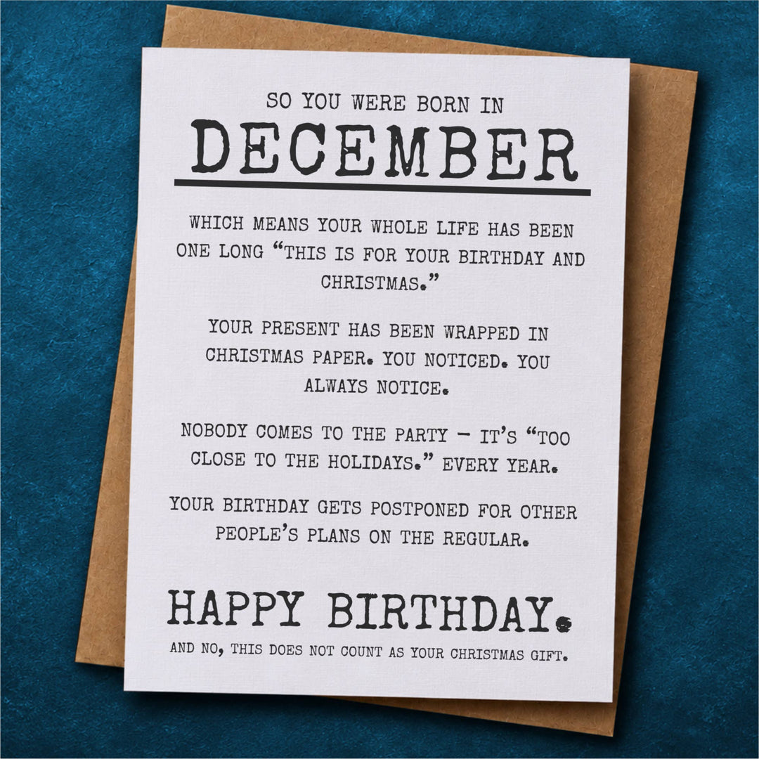 A humorous Christmas birthday card with black text on a white background, placed on top of a brown kraft envelope.