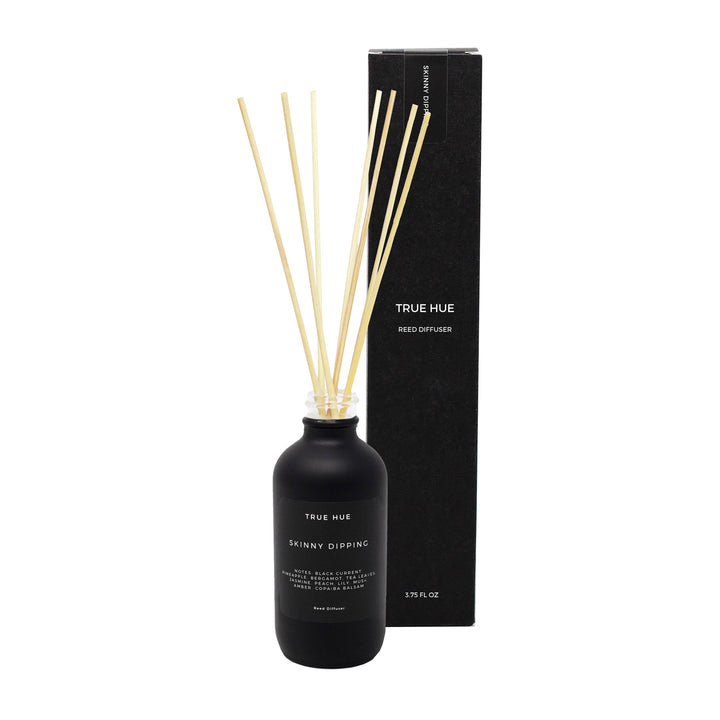 True Hue Skinny Dipping diffuser in a black bottle with white lettering, with seven reeds inserted, next to its black box.