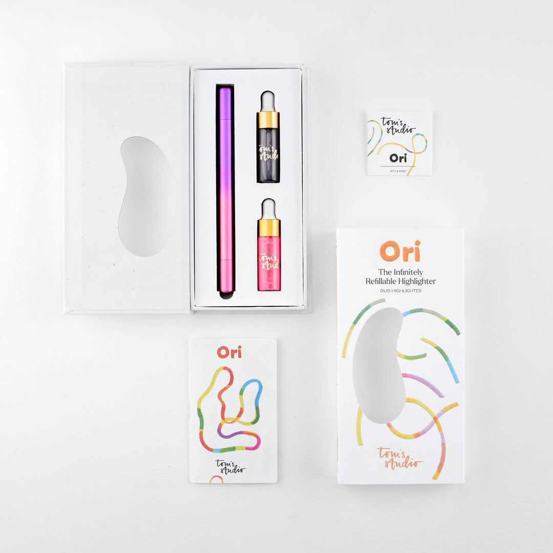 Opened package of the purple-pink pen with the pen and two containers of ink next to its cover and a booklet.