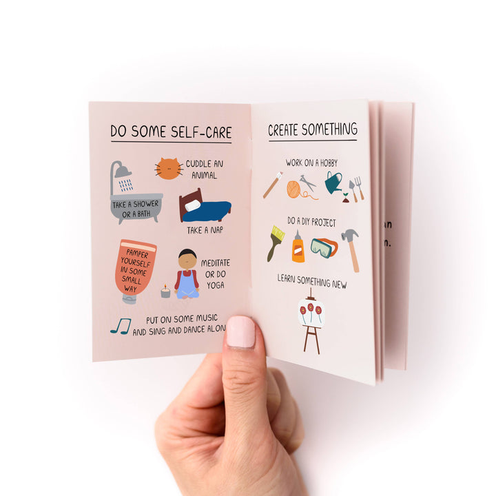Hand holding a small book with with titles "Do Some Self-Care" and "Create Somethingl" with several examples of each.
