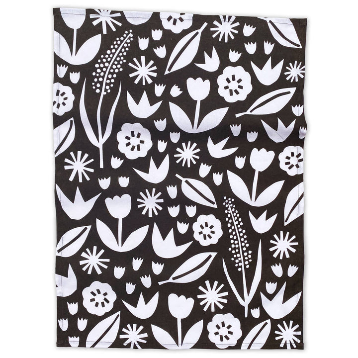 White images of flowers and petal shapes on a black cotton kitchen towel.