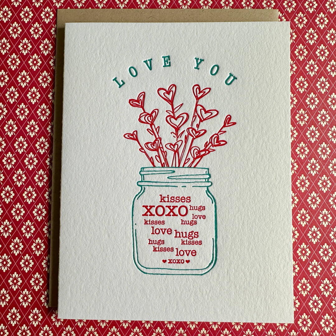 Short mason jar with bouquet of heart shaped flowers and stamped with words XOXO, kisses, hugs, love. Red text on white cardstock.