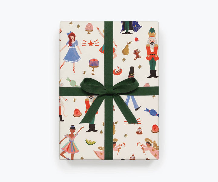 Package wrapped in off-white paper with images from the Nutcracker ballet, and tied with a green ribbon.