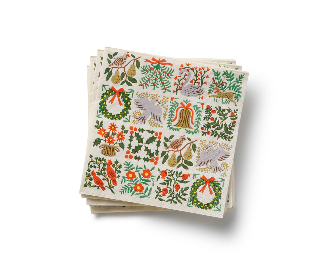 Paper napkins with holiday images of wreaths, pears, cardinals, and florals, organized in a grid, much like a quilt.