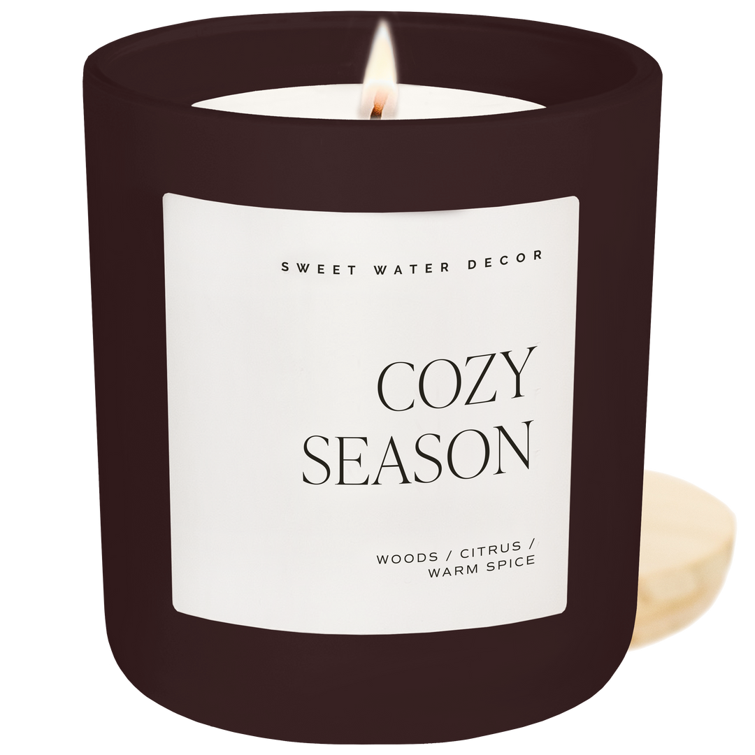 Lighted candle in brown jar with 'Cozy Season' label 