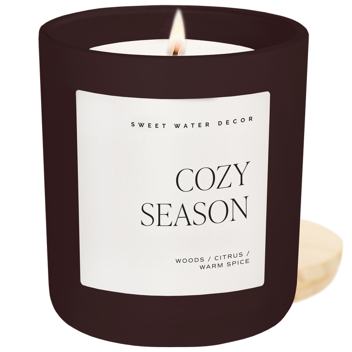 Lighted candle in brown jar with 'Cozy Season' label 