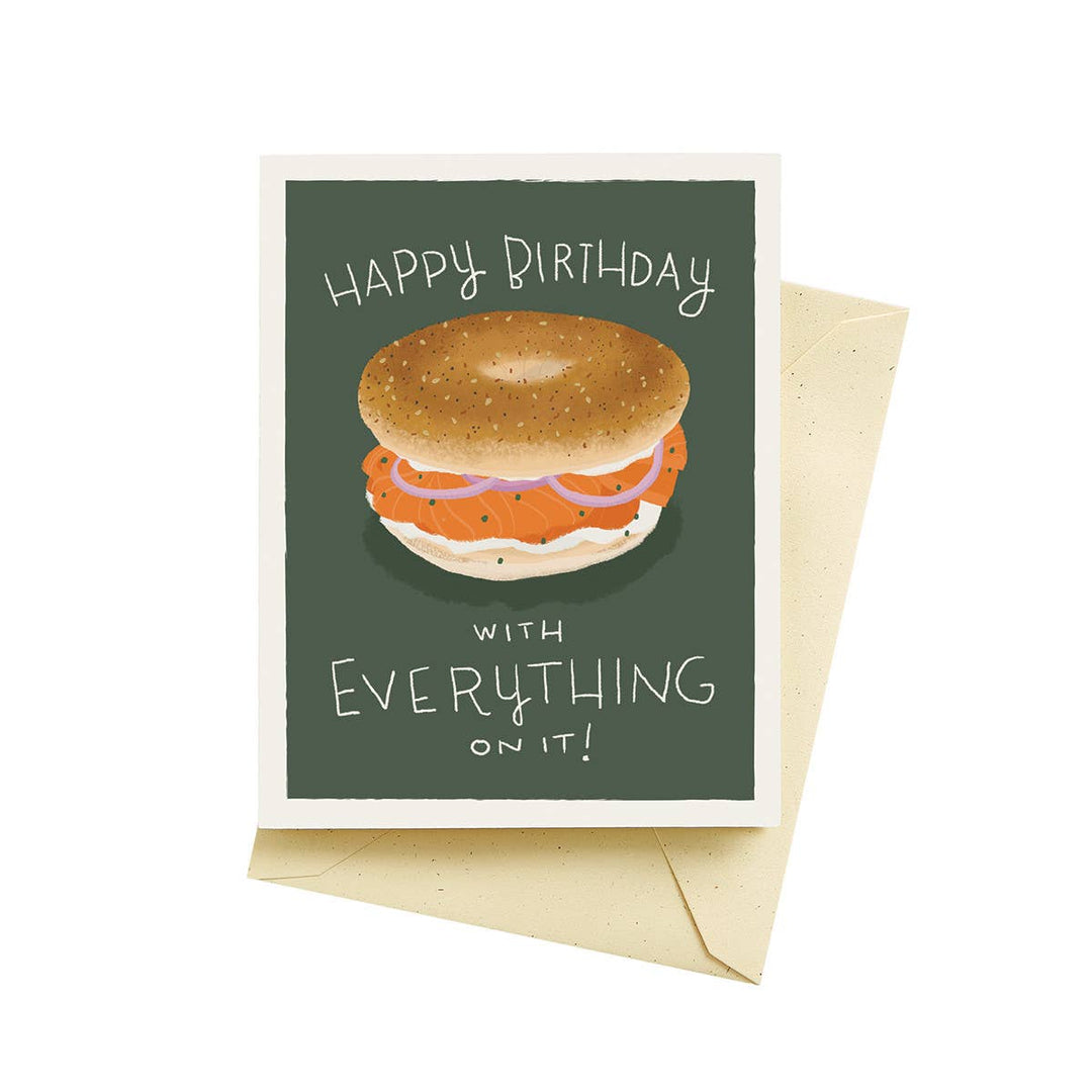 Bagel with lox, cream cheese and red onion between birthday greetings written in white on a green background.