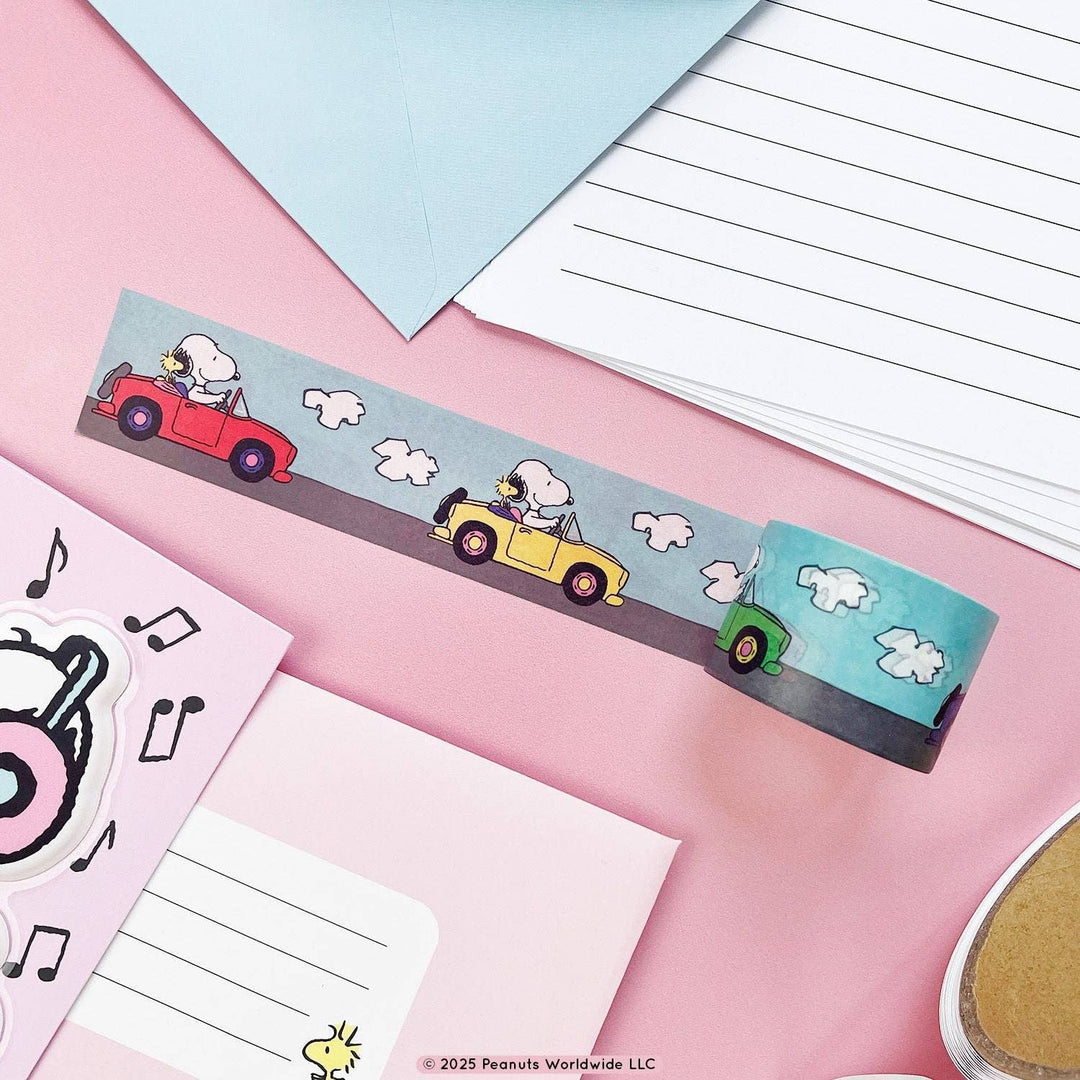 Snoopy washi taped unrolled to show Snoopy driving two cars, one red and one yellow with clouds overhead.