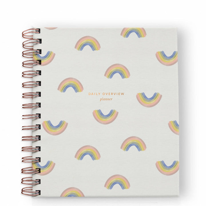 Cover of daily planner with a pattern of small rainbows and a gold spiral binding on the left side.