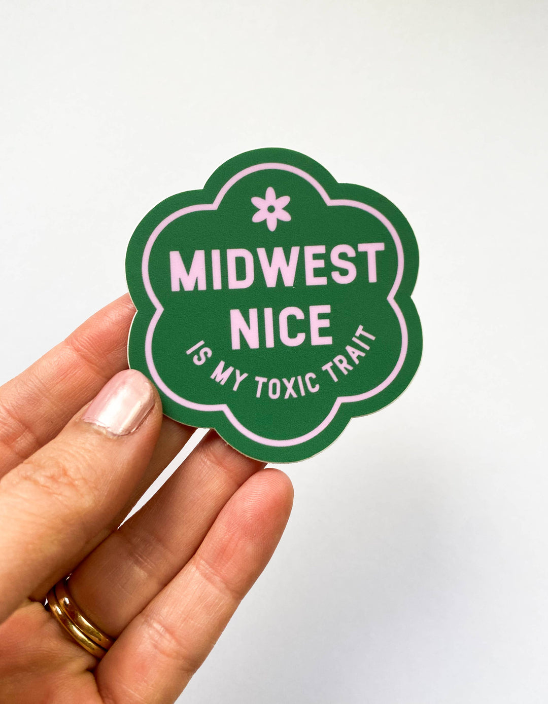 Hand holding a green sticker with 'Midwest Nice is my toxic trait' text.