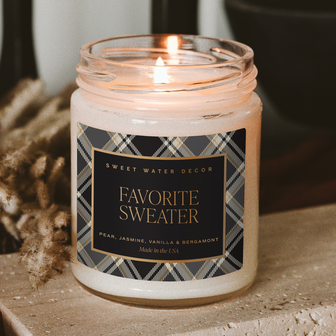 Lighted candle in a jar with a plaid label, placed on a stone surface