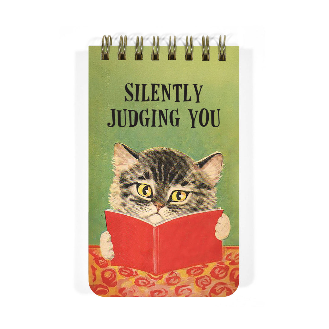 Green notebook cover with illustration of a cat looking over a book that it's holding under the text Silently Judging You' 
