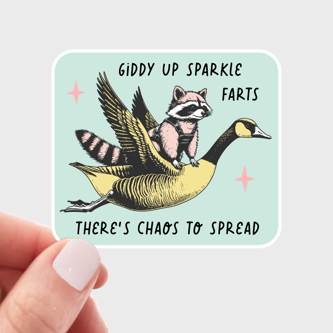 Sticker with a raccoon on a goose and humorous text, held by a hand.