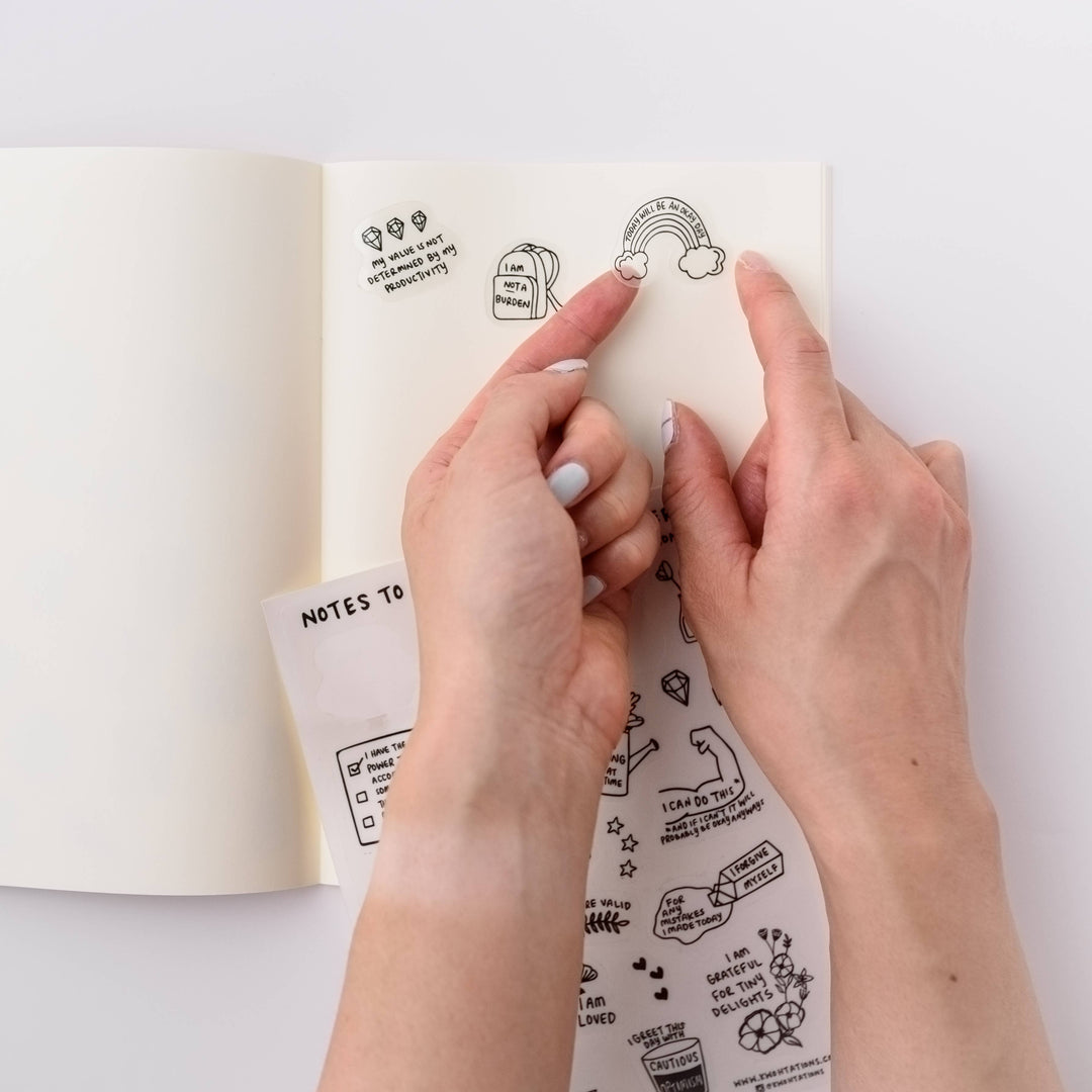 Hands applying a sticker to a notebook page.