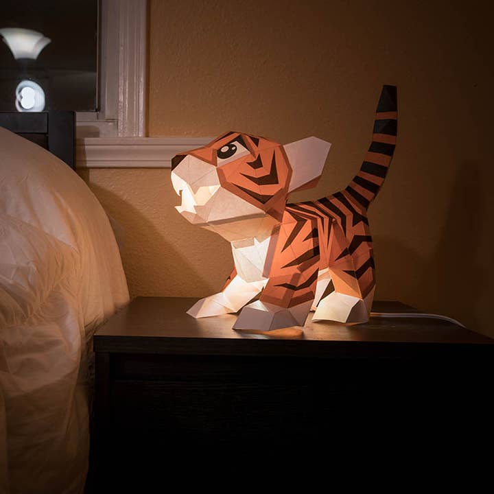 An orange origami tiger cub with brown stripes as a table lamp, lit from within. 