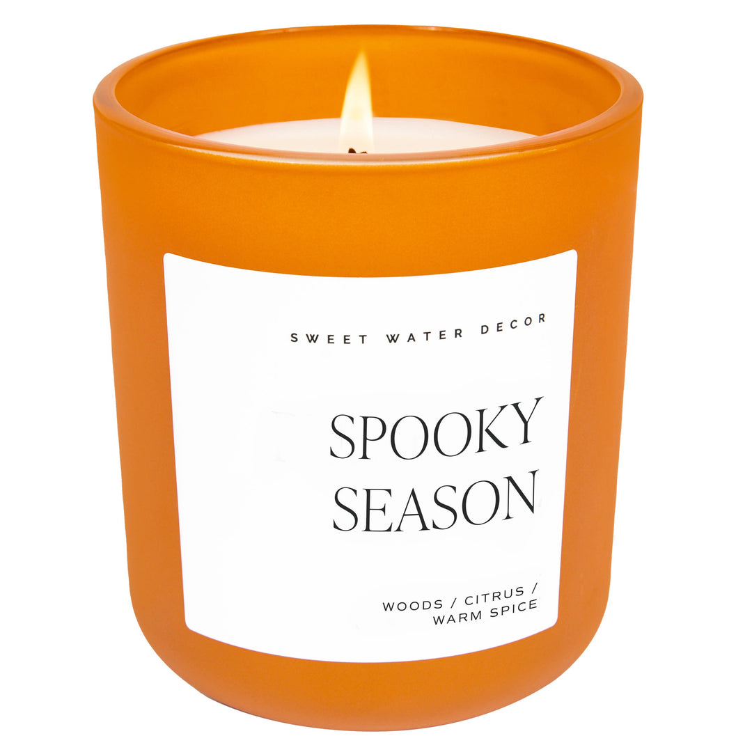 Scented soy candle in matte orange glass container. Label is Spooky Season  woods / citrus / warm spice