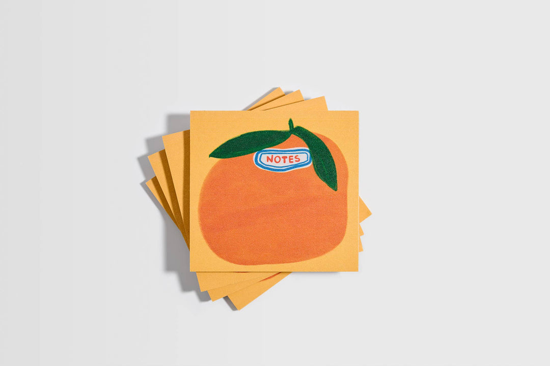 Stack of sticky notes with a large orange with green leaves and a label that says 'notes.'