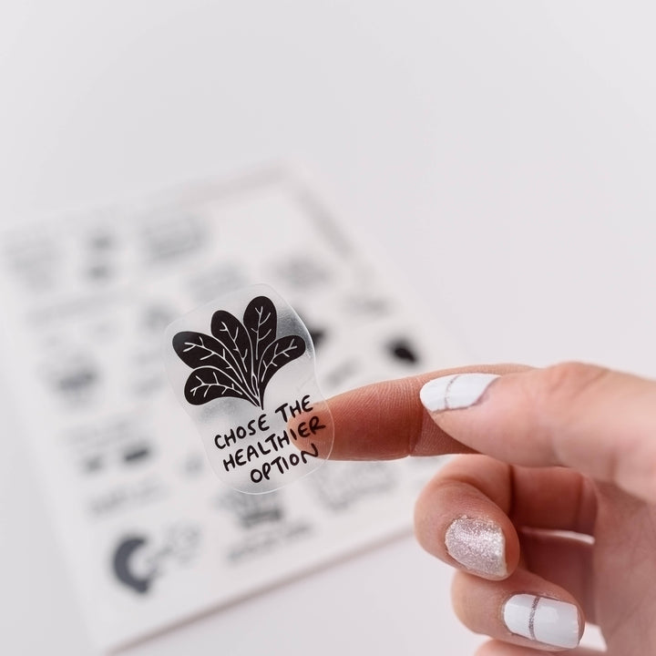 Hand holding a clear vinyl sticker with a leaf design and the text "Chose he healthier option." 