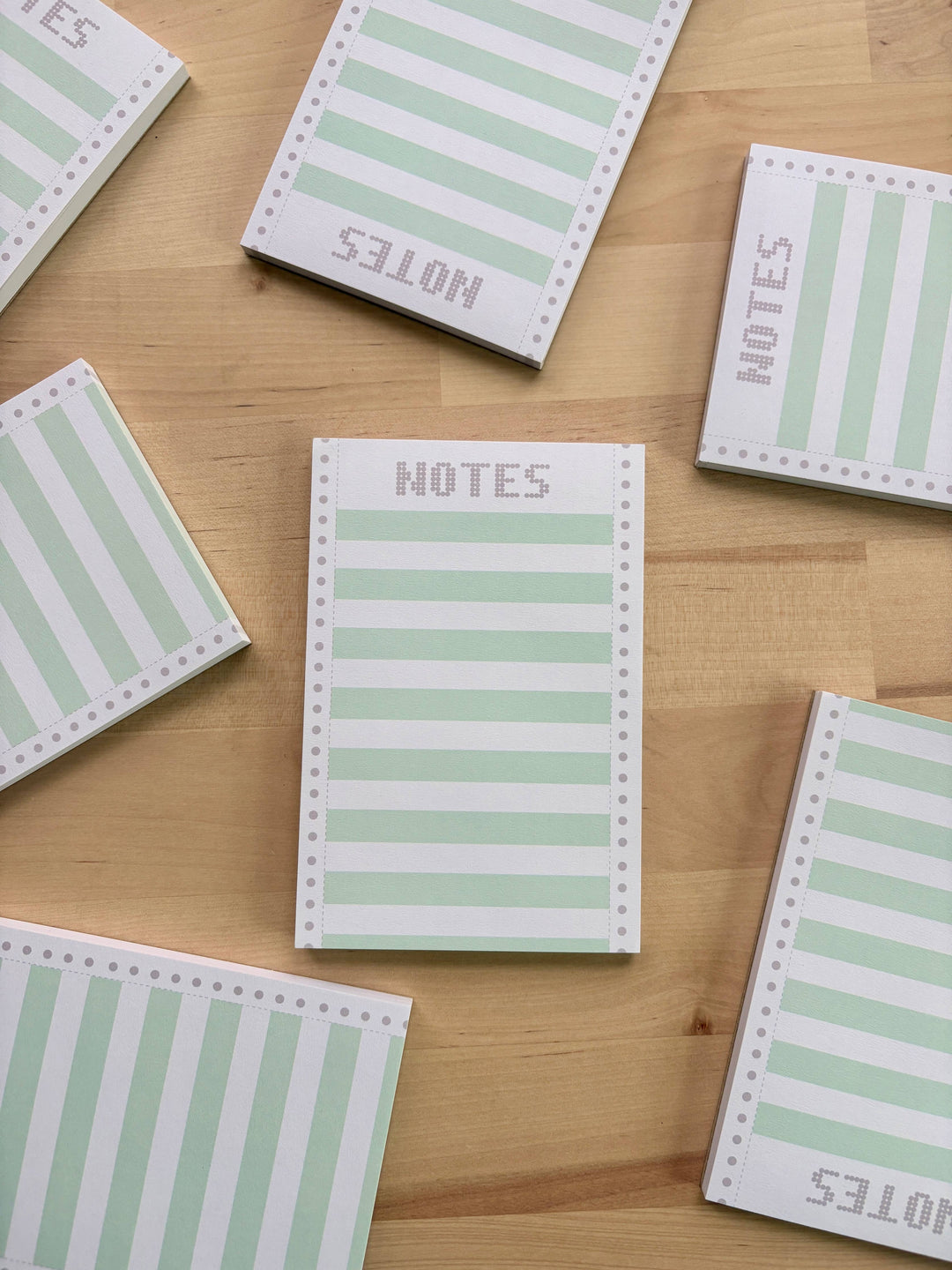 Several notepads that mimic old computer printer paper, green and white, lying on a wooden surface