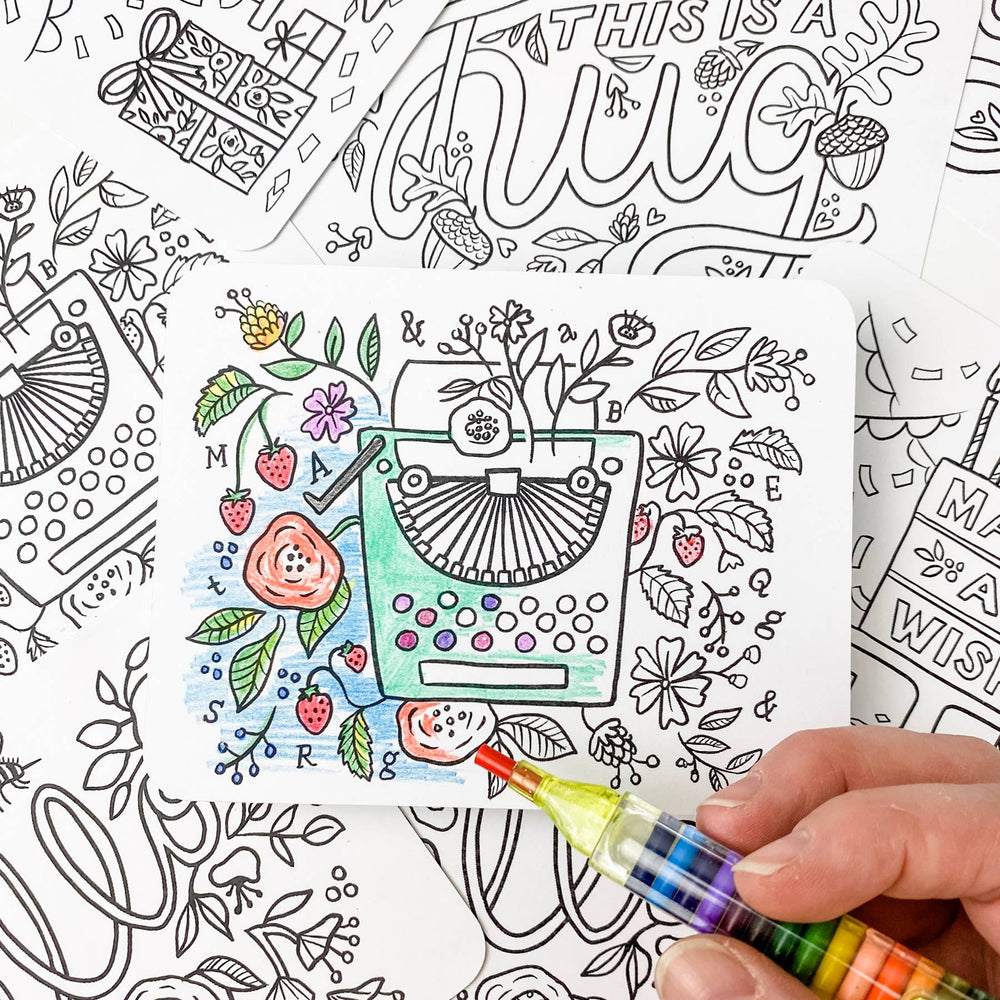 A hand holding the multi-colored marker coloring in one of the post card designs.