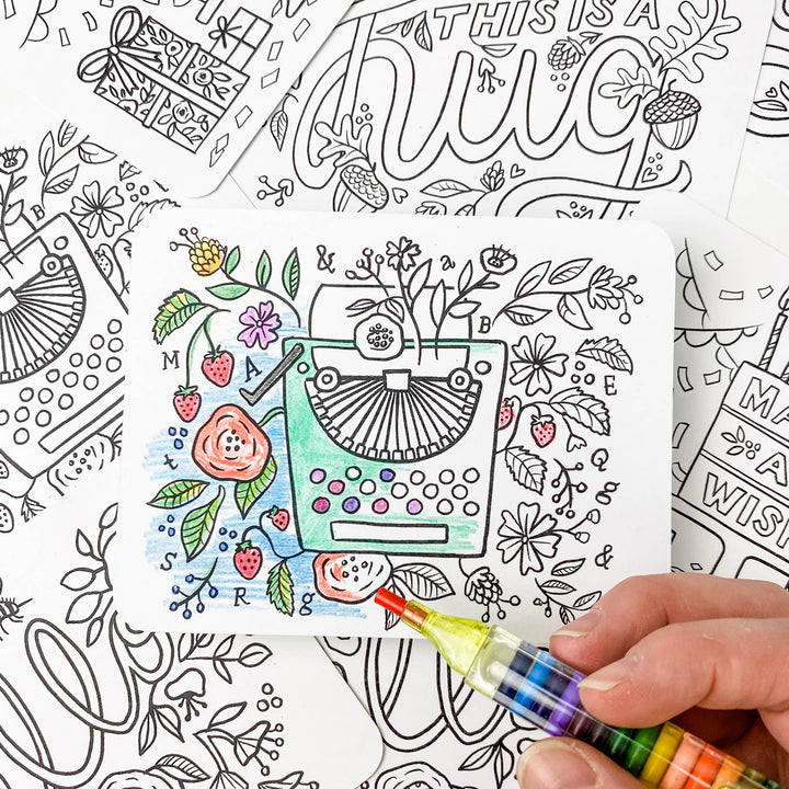 A hand holding the multi-colored marker coloring in one of the post card designs.