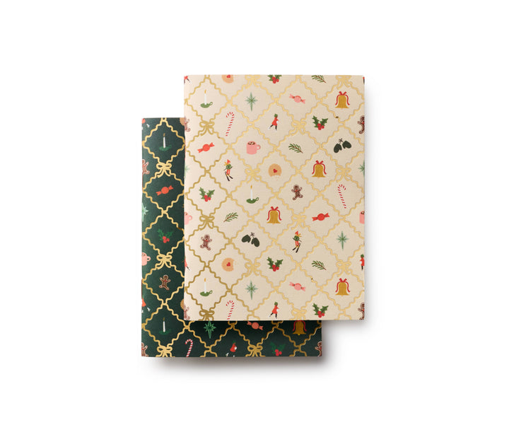 The covers of two patterned notebooks, each with a repeated pattern or holiday images in a grid of diamond shapes, the off-white cover is atop the dark green cover.