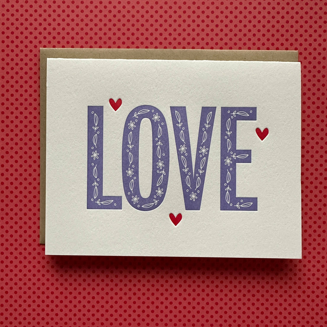 Big purple letters decorated with hand drawn leaves and flowers, with three red hearts. Red text on white cardstock. 