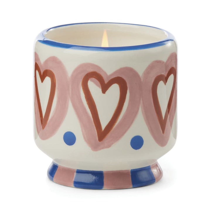 Footed ceramic vessel. The foot has alternating blue and pink squares. Around the outside of the vessel is a ring of large light and dark pink hearts separated at the bottom by a blue dot. 