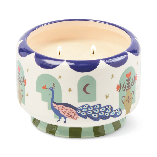 Four lit wicks in a ceramic candle holder with peacock design on an off-white background with blue scalloped trim around the top and green vertical stripes at the base.