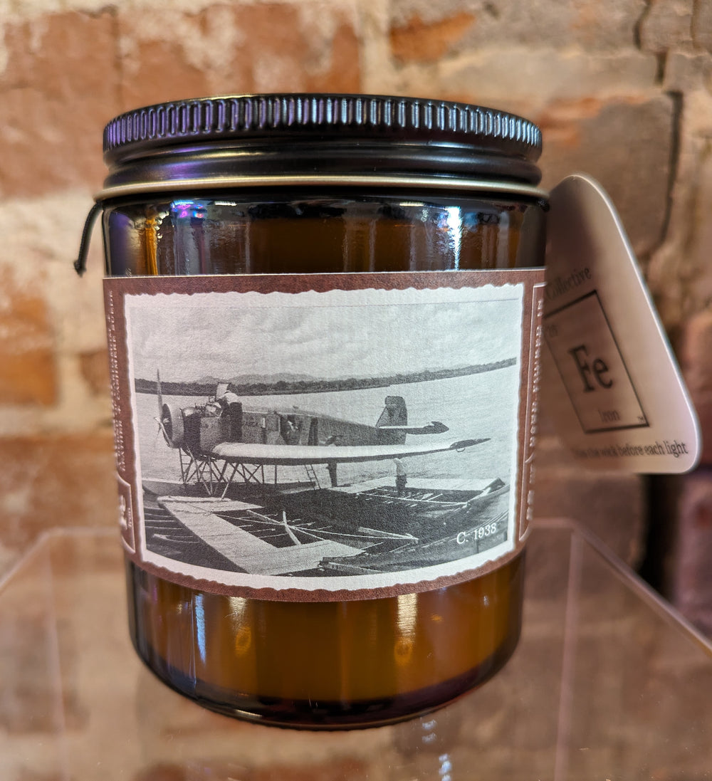 Scented coconut wax candle in a amber glass container with lid. Label has old-timey photo of a single-engine. plane.