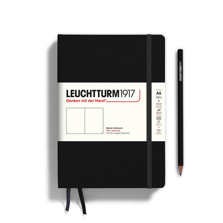 A black Leuchtturm1917 A5 plain page pocket notebook with a white front label and black elastic closure,  next to a black Leuchtturm1917 pencil.