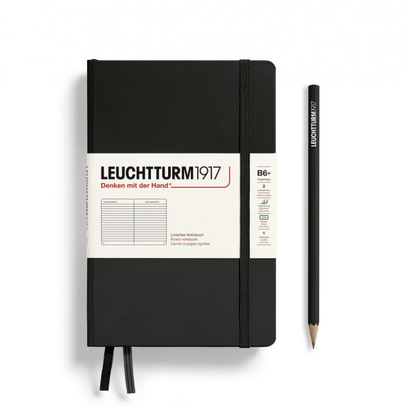 A black Leuchtturm1917 A5 ruled page pocket notebook with a white front label and black elastic closure,  next to a black Leuchtturm1917 pencil.