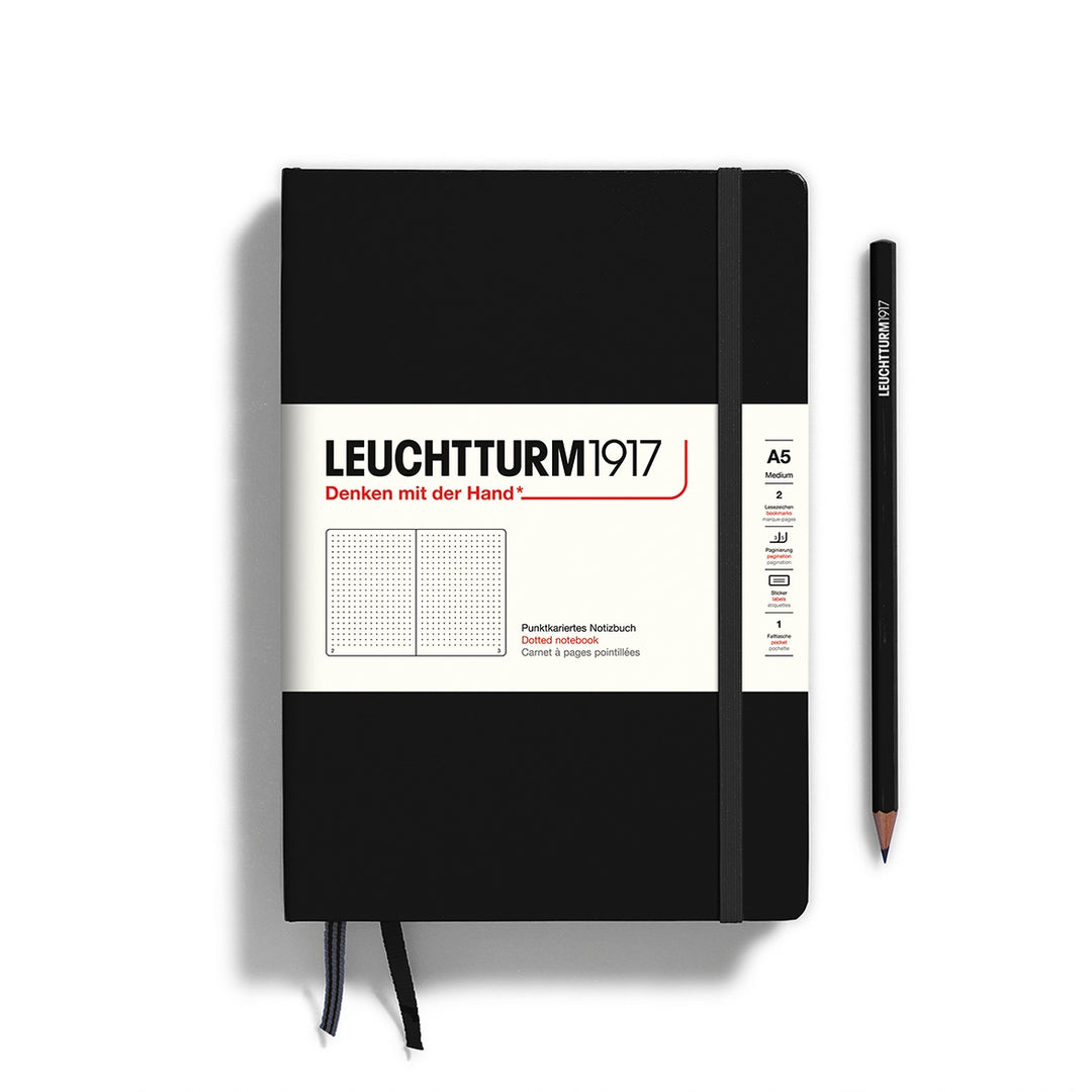 A black Leuchtturm1917 A5 dotted page pocket notebook with a white front label and black elastic closure,  next to a black Leuchtturm1917 pencil.