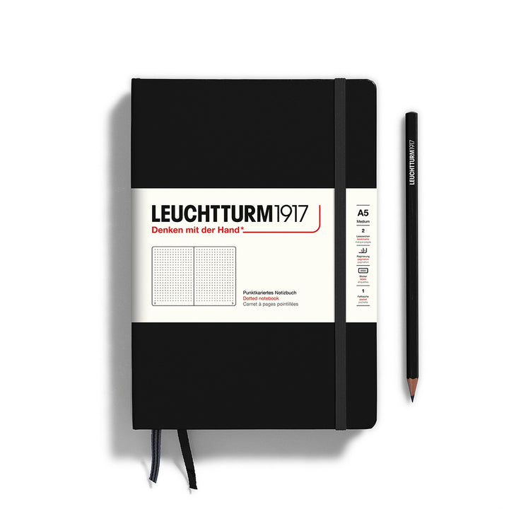 A black Leuchtturm1917 A5 dotted page pocket notebook with a white front label and black elastic closure,  next to a black Leuchtturm1917 pencil.