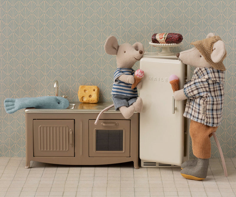 Tableau of a Maileg kitchen with a boy mouse sitting on the kitchen counter and a father mouse reaching into the refrigerator.